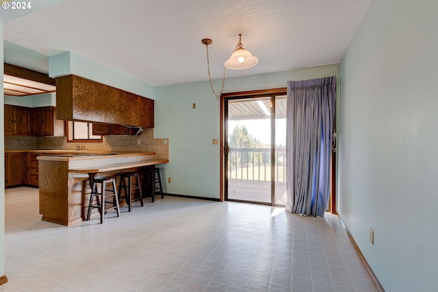 kitchen with kitchen peninsula, decorative backsplash, hanging light fixtures, and a kitchen bar