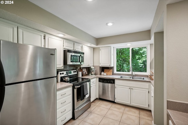 kitchen with sink, light tile patterned floors, appliances with stainless steel finishes, white cabinetry, and tasteful backsplash