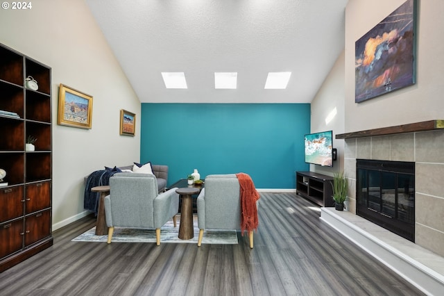 living room featuring lofted ceiling, dark wood-type flooring, a tile fireplace, and a textured ceiling