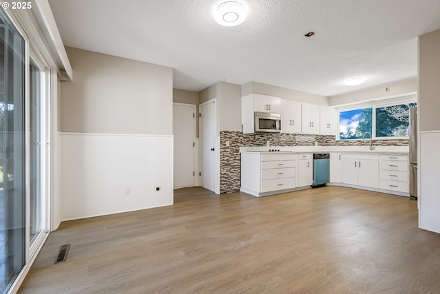 kitchen featuring appliances with stainless steel finishes, light wood-type flooring, a textured ceiling, and white cabinets