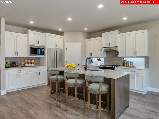 kitchen featuring appliances with stainless steel finishes, light hardwood / wood-style floors, white cabinets, decorative backsplash, and a center island with sink