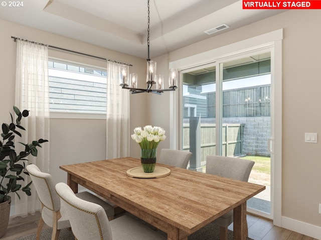 dining room with a chandelier, a tray ceiling, and light wood-type flooring