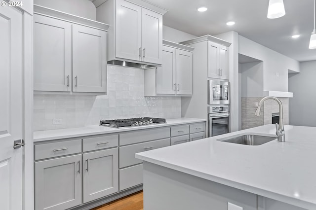 kitchen featuring tasteful backsplash, sink, hanging light fixtures, light hardwood / wood-style floors, and stainless steel appliances