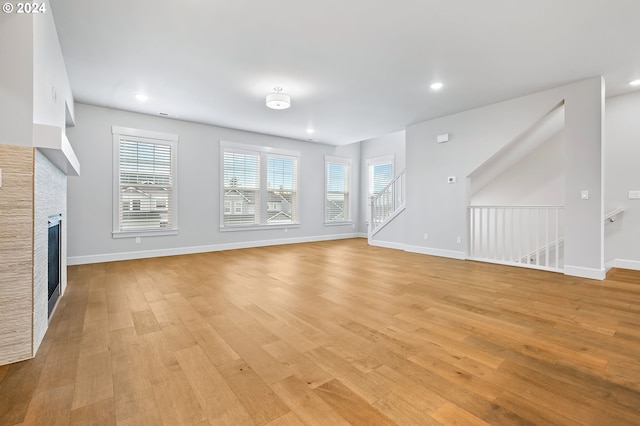 unfurnished living room featuring a healthy amount of sunlight, a stone fireplace, and light wood-type flooring