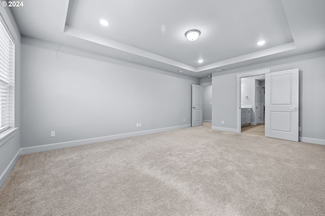 unfurnished bedroom with multiple windows, light carpet, and a tray ceiling