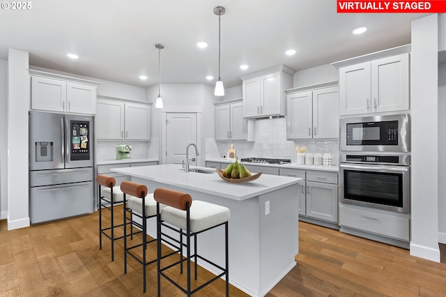 kitchen featuring backsplash, pendant lighting, a center island with sink, sink, and appliances with stainless steel finishes