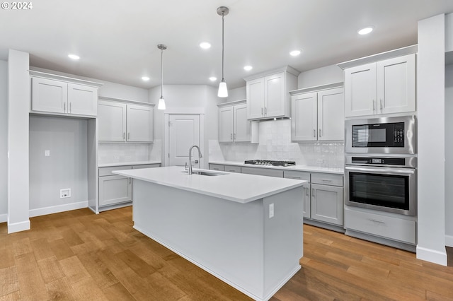 kitchen featuring sink, decorative light fixtures, appliances with stainless steel finishes, an island with sink, and light hardwood / wood-style floors