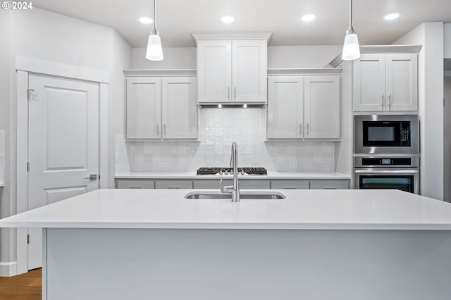 kitchen featuring pendant lighting, white cabinetry, appliances with stainless steel finishes, and a kitchen island with sink