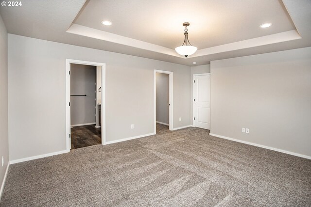 unfurnished bedroom featuring ensuite bath, a tray ceiling, dark carpet, and a spacious closet