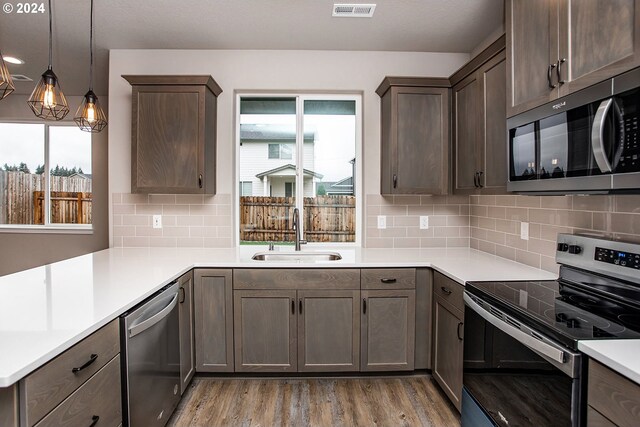 kitchen with sink, stainless steel appliances, backsplash, wood-type flooring, and decorative light fixtures