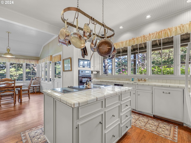 kitchen featuring black appliances, a center island, decorative light fixtures, light hardwood / wood-style floors, and tile countertops