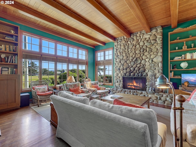 living room featuring beam ceiling, a stone fireplace, built in shelves, hardwood / wood-style floors, and wooden ceiling