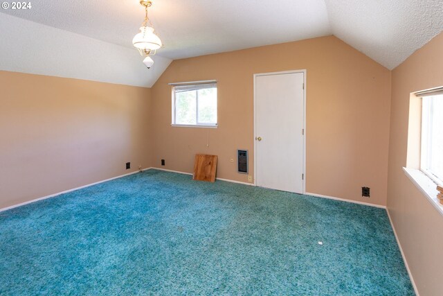 carpeted spare room featuring lofted ceiling, a textured ceiling, and heating unit