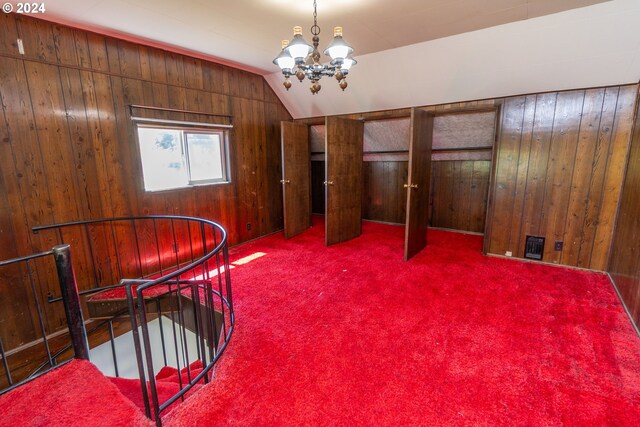 interior space featuring carpet, wood walls, an inviting chandelier, and lofted ceiling