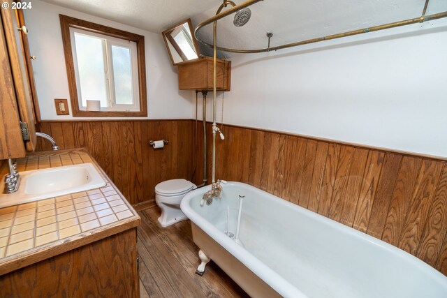 bathroom with toilet, hardwood / wood-style floors, a textured ceiling, wood walls, and sink