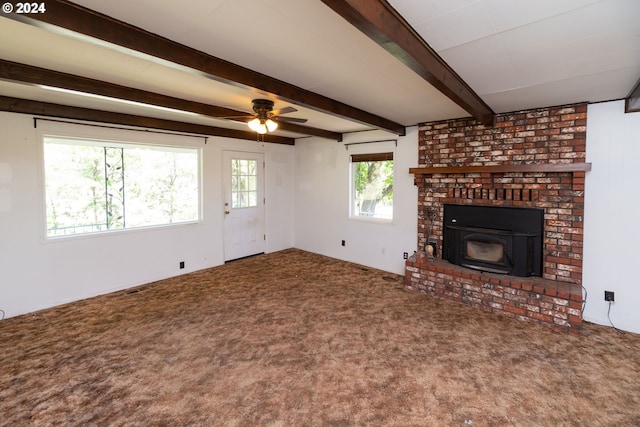 unfurnished living room with ceiling fan, carpet floors, beamed ceiling, and a brick fireplace