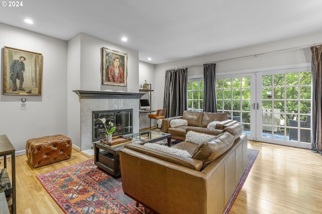 living room with light wood-type flooring, french doors, and a tiled fireplace