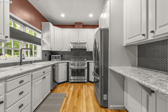 kitchen featuring light stone countertops, appliances with stainless steel finishes, tasteful backsplash, light hardwood / wood-style flooring, and white cabinetry