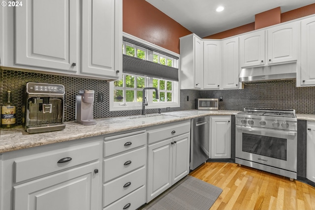 kitchen with decorative backsplash, appliances with stainless steel finishes, sink, white cabinets, and light hardwood / wood-style floors