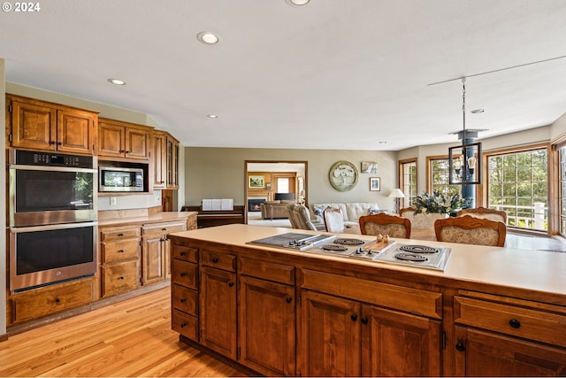 kitchen with light wood-type flooring, appliances with stainless steel finishes, lofted ceiling, and decorative light fixtures