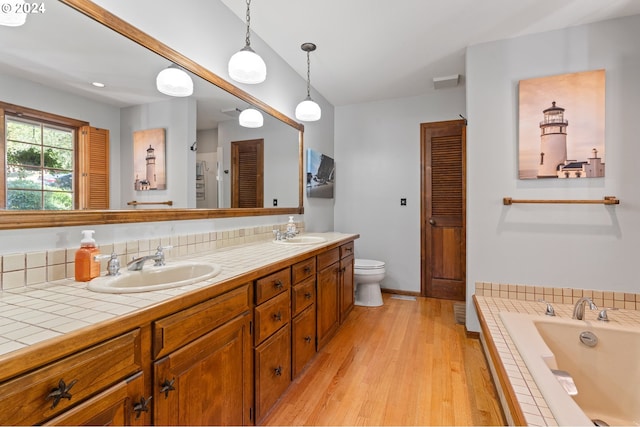 bathroom featuring a relaxing tiled tub, hardwood / wood-style flooring, vanity, and toilet