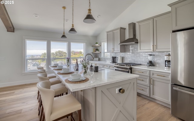 kitchen with a kitchen island with sink, appliances with stainless steel finishes, sink, wall chimney range hood, and lofted ceiling