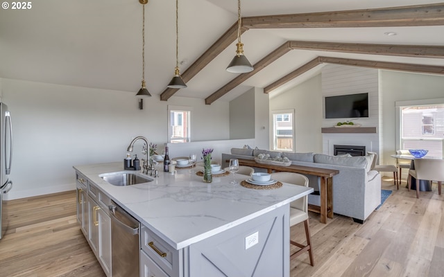 kitchen with sink, decorative light fixtures, light stone countertops, a center island with sink, and appliances with stainless steel finishes