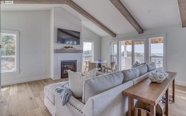 living room featuring lofted ceiling with beams, a large fireplace, a wealth of natural light, and light hardwood / wood-style flooring