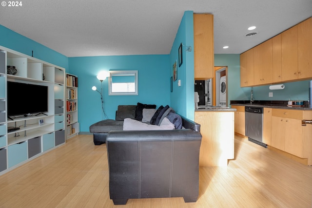 living room with a textured ceiling, light wood-type flooring, and stacked washer and clothes dryer