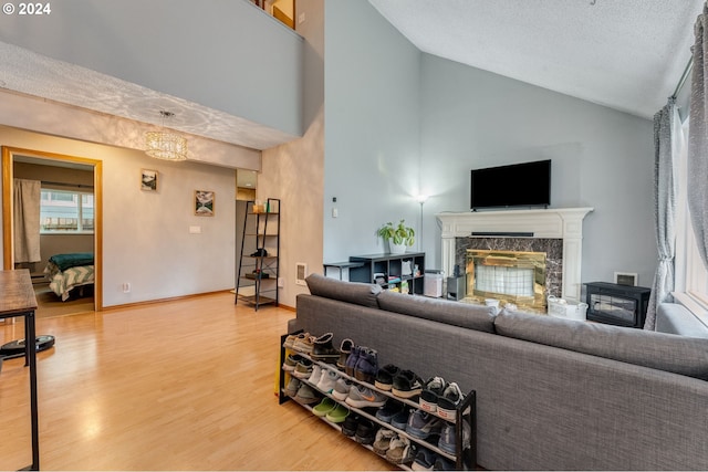 living room featuring high vaulted ceiling, a high end fireplace, an inviting chandelier, hardwood / wood-style flooring, and a textured ceiling