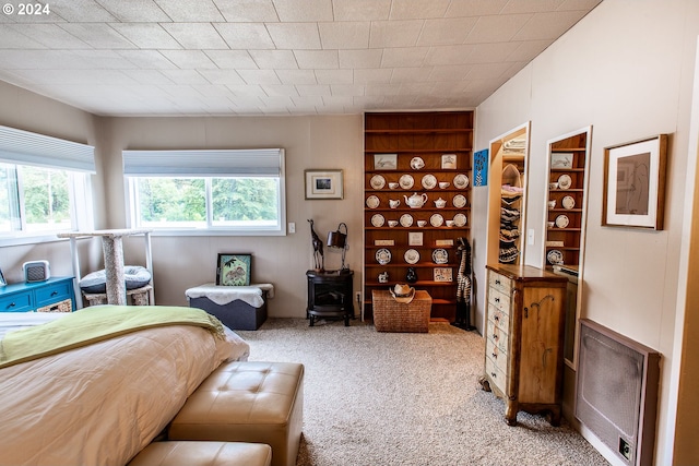 bedroom with multiple windows, heating unit, and light colored carpet