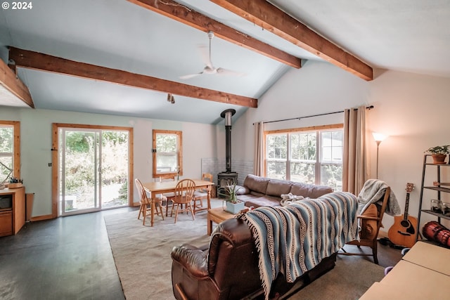 living room with ceiling fan, a wood stove, and vaulted ceiling with beams