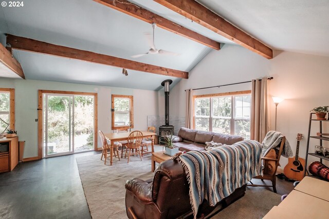 living room featuring a healthy amount of sunlight, a wood stove, vaulted ceiling with beams, and ceiling fan