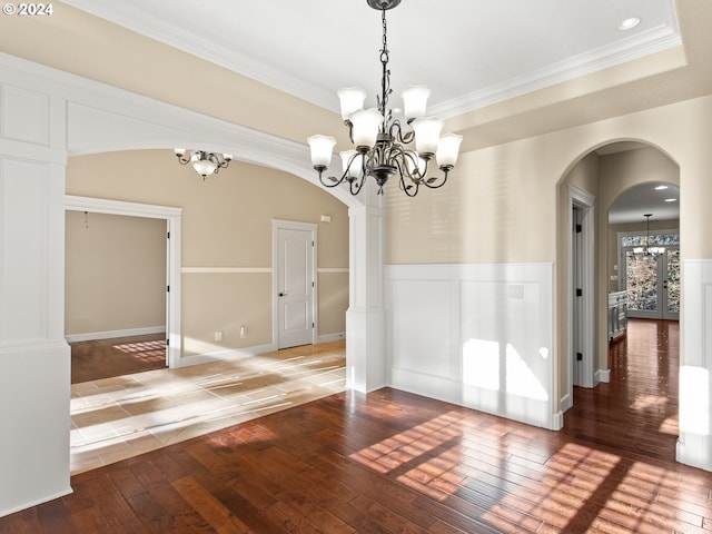 unfurnished dining area with arched walkways, a notable chandelier, a wainscoted wall, wood finished floors, and crown molding