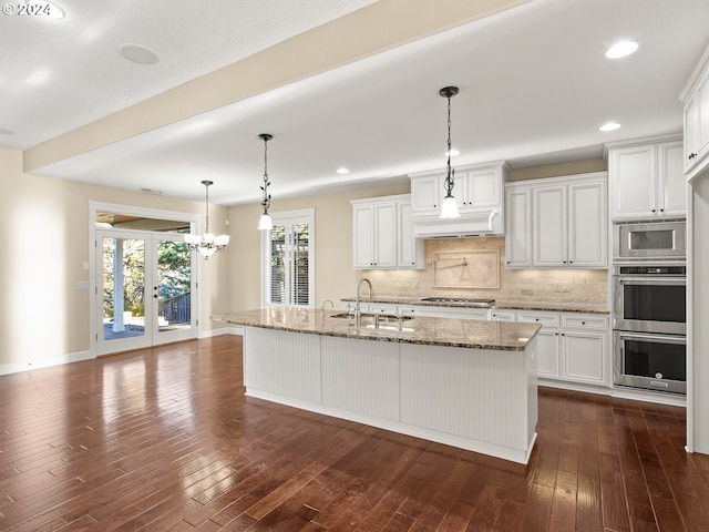 kitchen with appliances with stainless steel finishes, white cabinets, a center island with sink, and light stone countertops