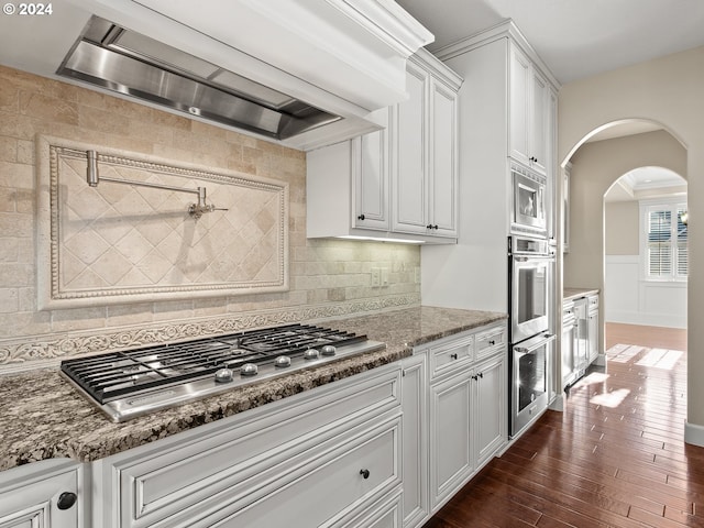 kitchen with wall chimney range hood, appliances with stainless steel finishes, white cabinetry, and dark stone countertops