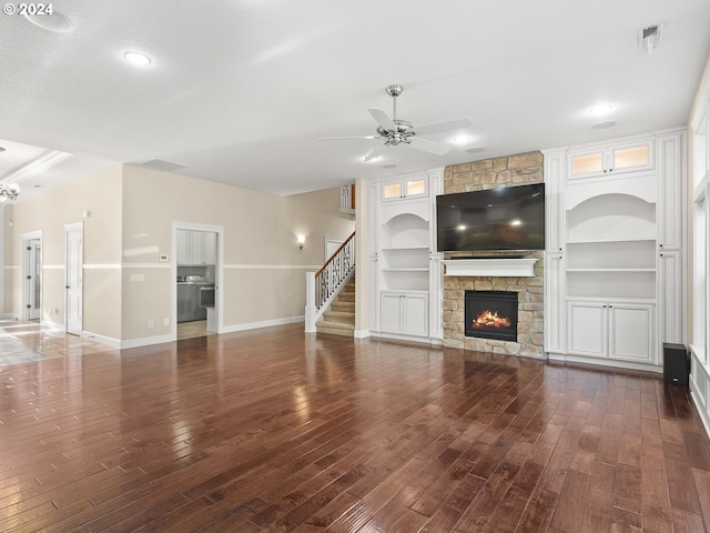 unfurnished living room with ceiling fan, built in shelves, baseboards, stairway, and dark wood-style floors