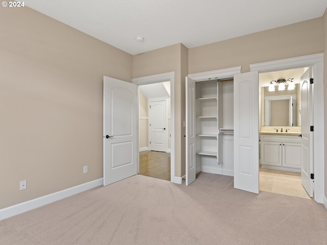 unfurnished bedroom with connected bathroom, light colored carpet, a sink, baseboards, and a closet