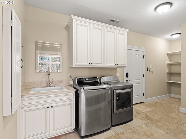 clothes washing area with visible vents, cabinet space, washing machine and dryer, a sink, and a textured ceiling