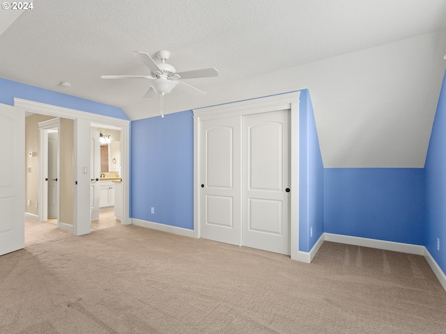 unfurnished bedroom with a textured ceiling, light carpet, baseboards, vaulted ceiling, and a closet