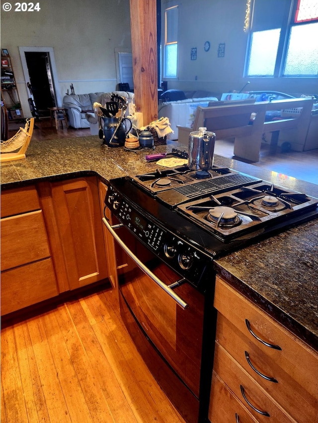 kitchen featuring light wood finished floors, black gas range, brown cabinets, and a wealth of natural light