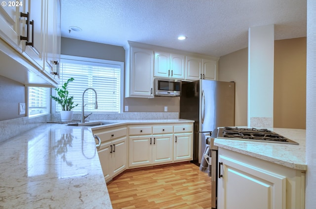 kitchen featuring sink, stainless steel appliances, light hardwood / wood-style floors, a textured ceiling, and white cabinets