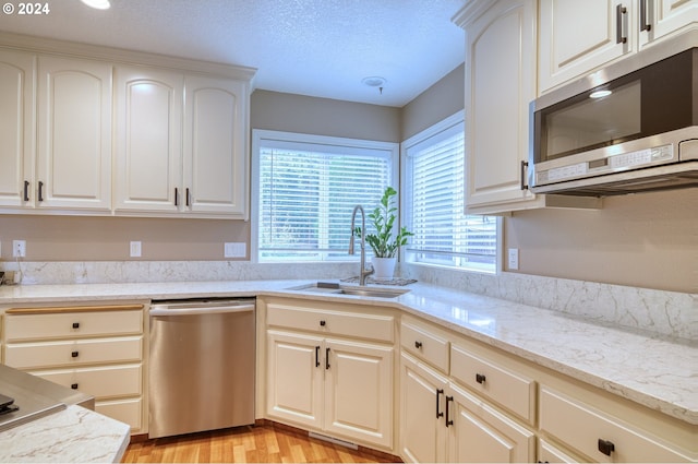 kitchen with light stone countertops, appliances with stainless steel finishes, light wood-type flooring, a textured ceiling, and sink