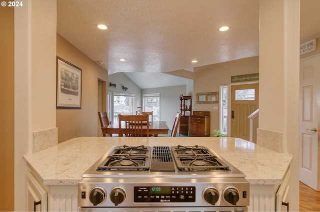 kitchen with a textured ceiling, light stone countertops, light hardwood / wood-style floors, and stainless steel range oven