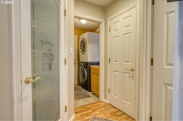 clothes washing area with a textured ceiling, cabinets, light wood-type flooring, and stacked washer and dryer