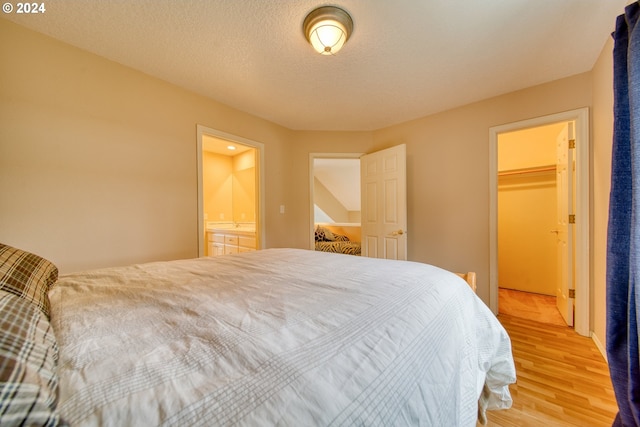 bedroom with a walk in closet, light hardwood / wood-style flooring, a textured ceiling, connected bathroom, and a closet