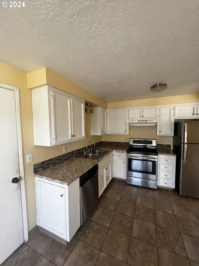 kitchen with stainless steel appliances, dark tile patterned flooring, a textured ceiling, sink, and white cabinetry