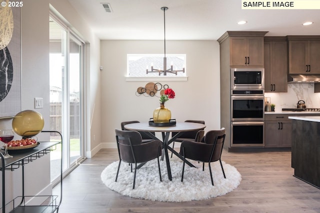 kitchen with tasteful backsplash, decorative light fixtures, light hardwood / wood-style flooring, and appliances with stainless steel finishes