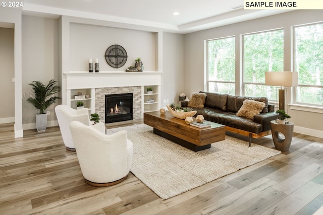 living room featuring built in features, hardwood / wood-style flooring, and a stone fireplace