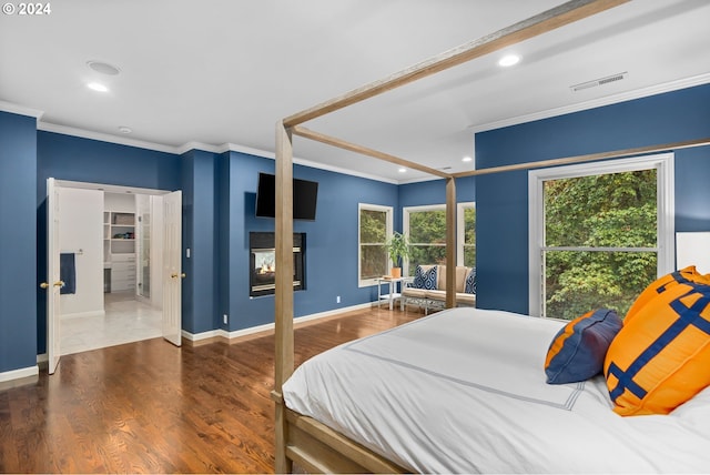 bedroom featuring a multi sided fireplace, ornamental molding, and dark hardwood / wood-style flooring